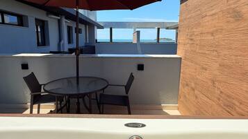 A terrace with a table and chairs, an umbrella, and a view of the sea.