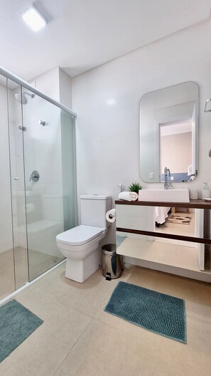 A modern bathroom with a glass shower enclosure, a toilet, a sink with a mirror, and a trash can.