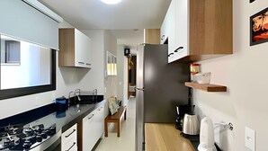 A modern kitchen with a gas stove, wooden cabinets, a stainless steel refrigerator, and a coffee maker. - Res Belvedere Beach Garden (Florianópolis)
