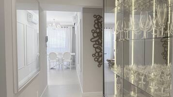 A corridor with a glass display case of wine glasses, a dining area with a chandelier, and a decorative wall piece.