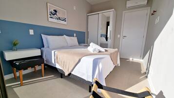 A hotel room with a bed, bedside table, chair, and a wall-mounted air conditioner.