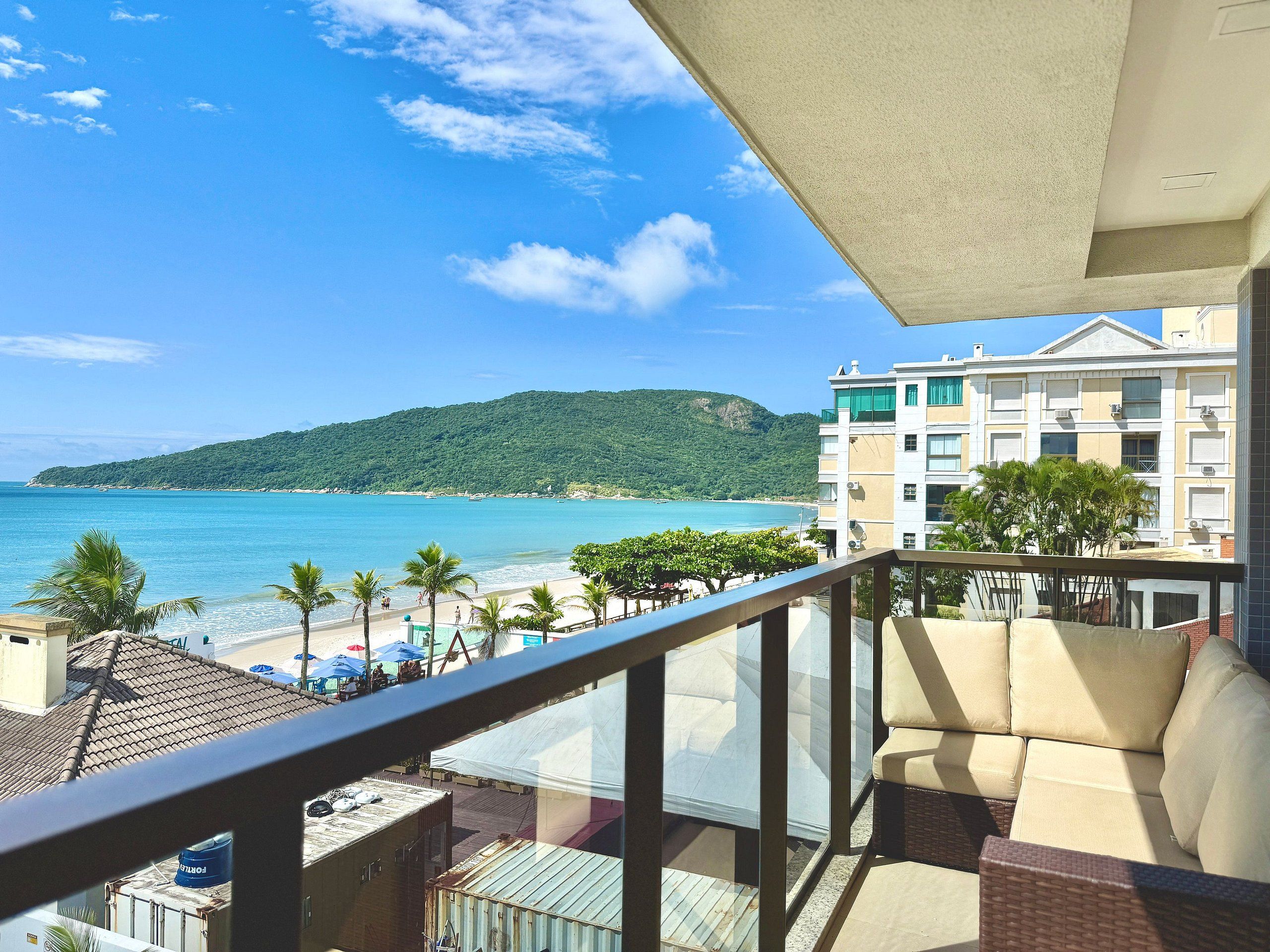 Un balcon avec vue sur une plage, une montagne et un bâtiment d’hôtel.