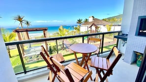 Un balcón con mesa y sillas de madera, con vista a una playa y al océano.