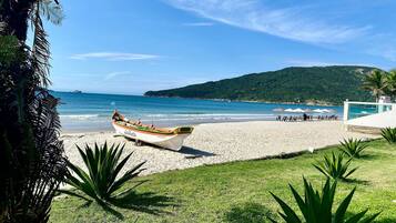 A boat named 'Galheta' on a beach with a grassy area, umbrellas, and a mountain in the background.