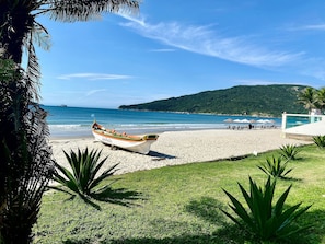 Un bote llamado 'Galheta' en una playa con zona de césped, sombrillas y una montaña al fondo.