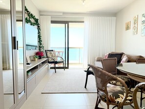 A modern living room with a balcony, wicker furniture, and a view of the sea. - Res Belvedere Beach Garden (Florianópolis)