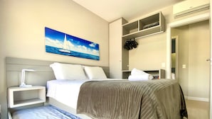 A hotel room with a bed, bedside table, lamp, and a painting of a sailboat on the wall.
