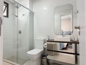 Un baño moderno con cabina de ducha de vidrio, inodoro, lavamanos y espejo.