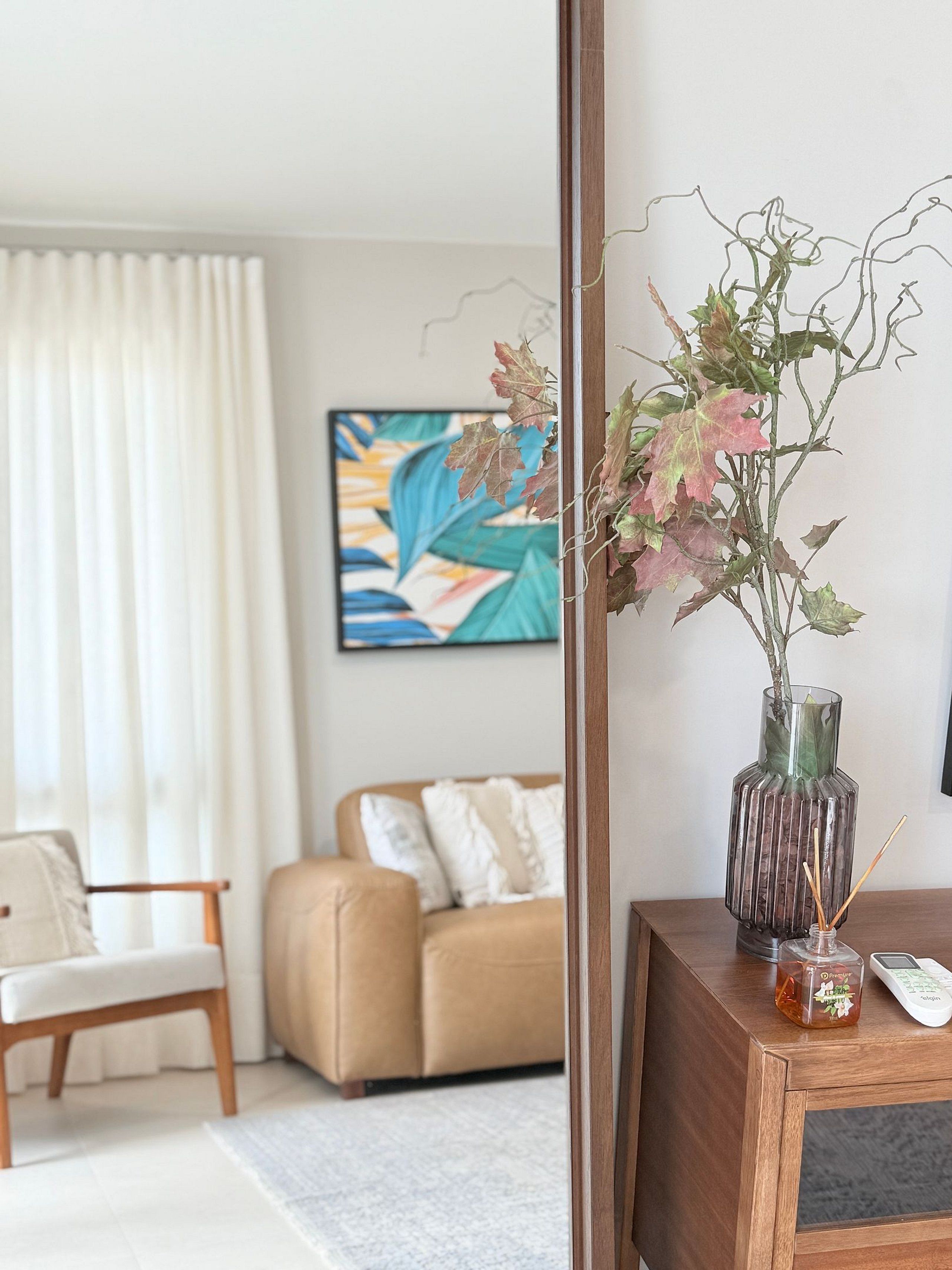 Een moderne woonkamer met een bank, een fauteuil, een houten bijzettafeltje met een vaas en een pot honing, en een schilderij aan de muur.