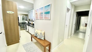 A hallway with a wooden bench, a rug, and a wall with three framed pictures. - Res Belvedere Beach Garden (Florianópolis)
