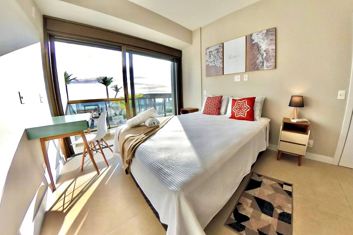 A modern hotel room with a large bed, a desk, and a balcony with a view.