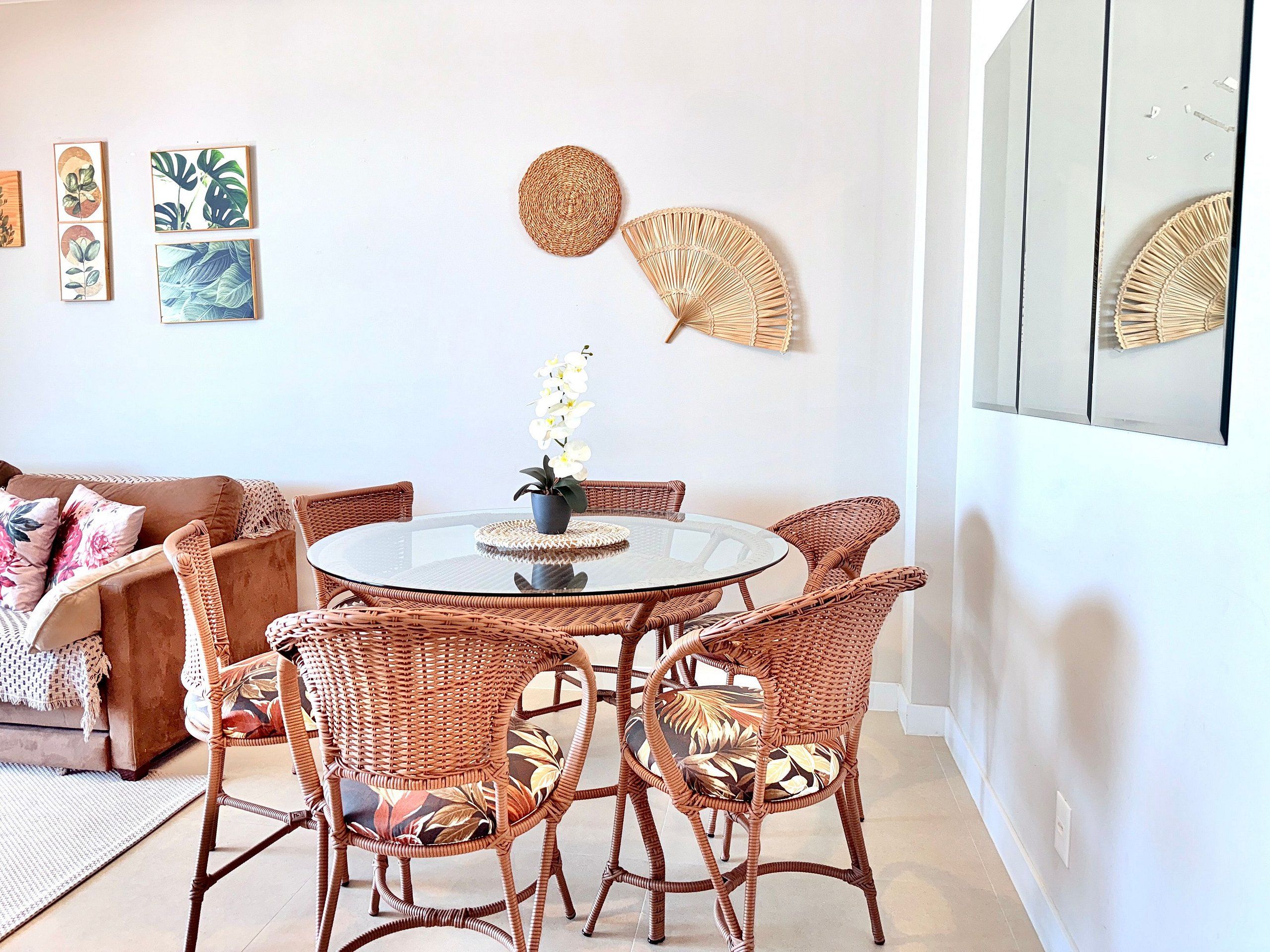 Uma sala de jantar com cadeiras de vime, uma mesa de vidro e um vaso com flores.