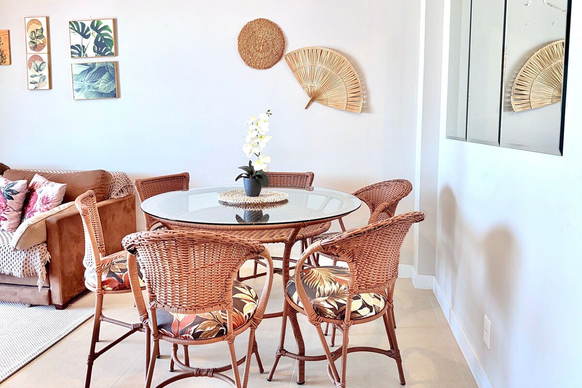 Een eetgedeelte met rieten stoelen, een glazen tafel en een vaas met bloemen.