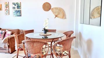 Uma sala de jantar com cadeiras de vime, uma mesa de vidro e um vaso com flores.
