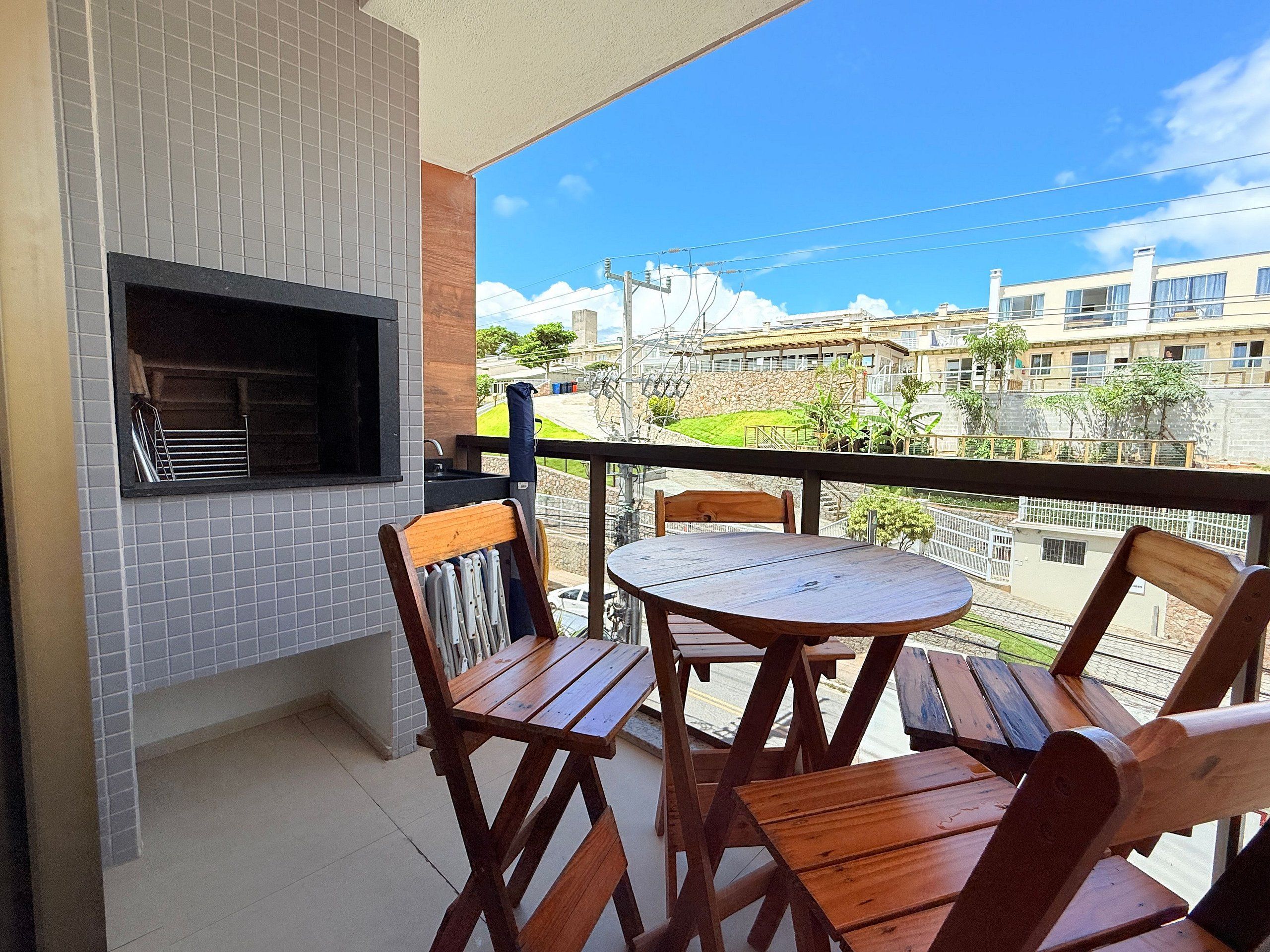 Een balkon met een barbecue, houten stoelen en een tafeltje.