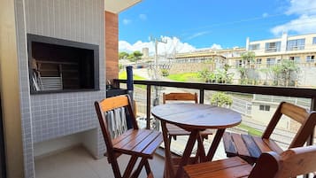 Een balkon met een barbecue, houten stoelen en een tafeltje.