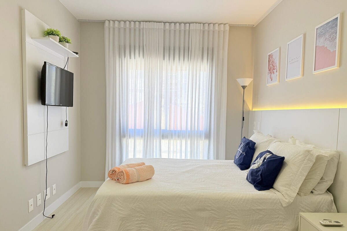 A hotel room with a bed, a TV mounted on the wall, a bedside table, and a lamp.