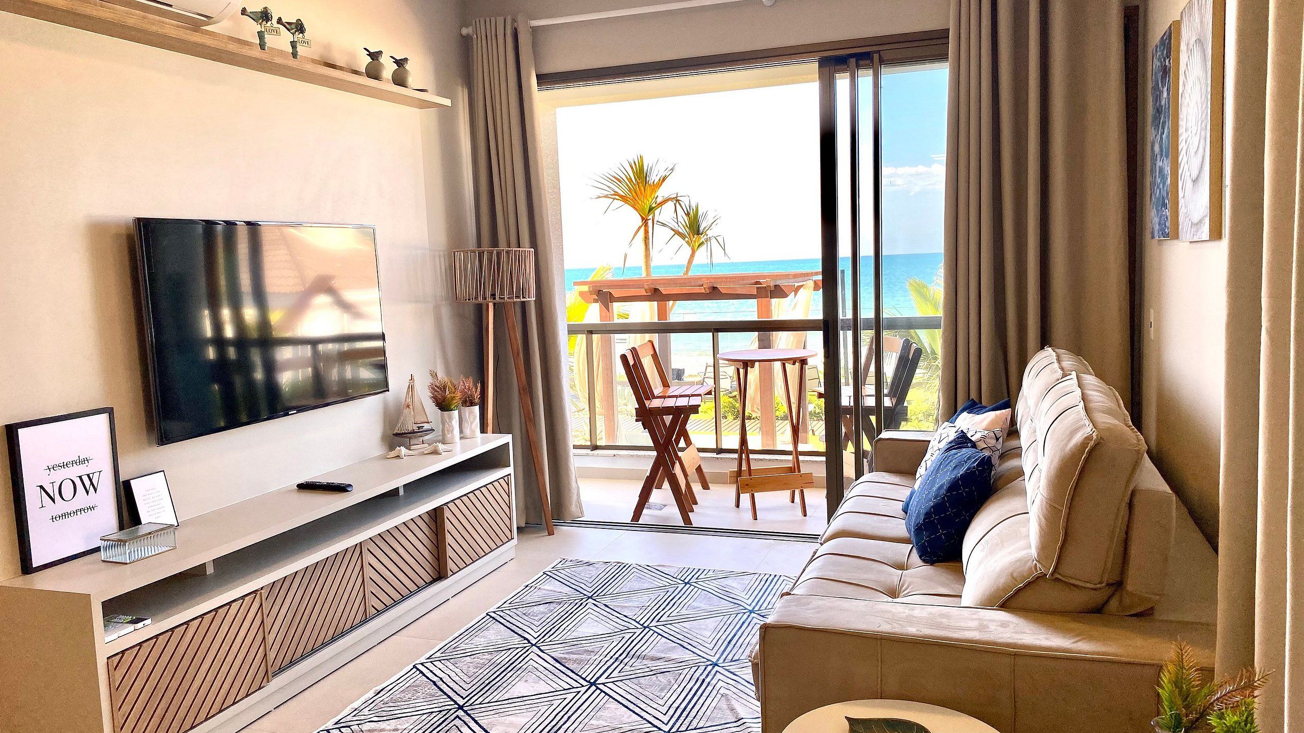 A modern living room with a TV, sofa, and balcony with a view of the sea.
