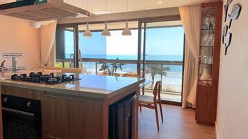 A modern kitchen with a central island, a dining area with a view of the ocean, and a wooden cabinet with glassware.