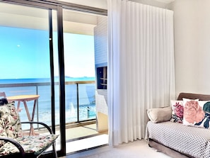 Una habitación con cama, una silla y vista al océano a través de una puerta corrediza.