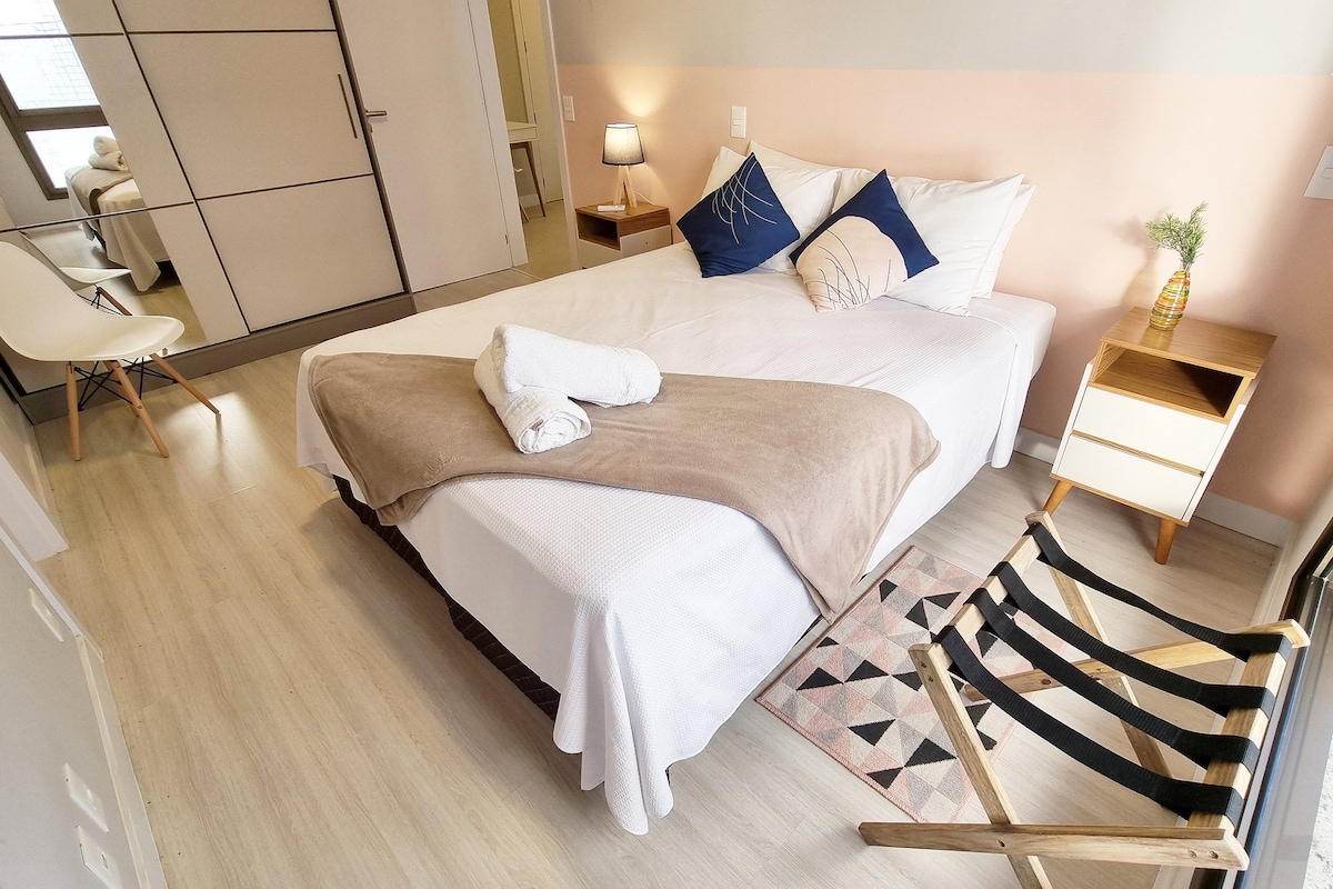 Una habitación de hotel con cama, una silla, una mesita de noche, una lámpara y una planta pequeña.