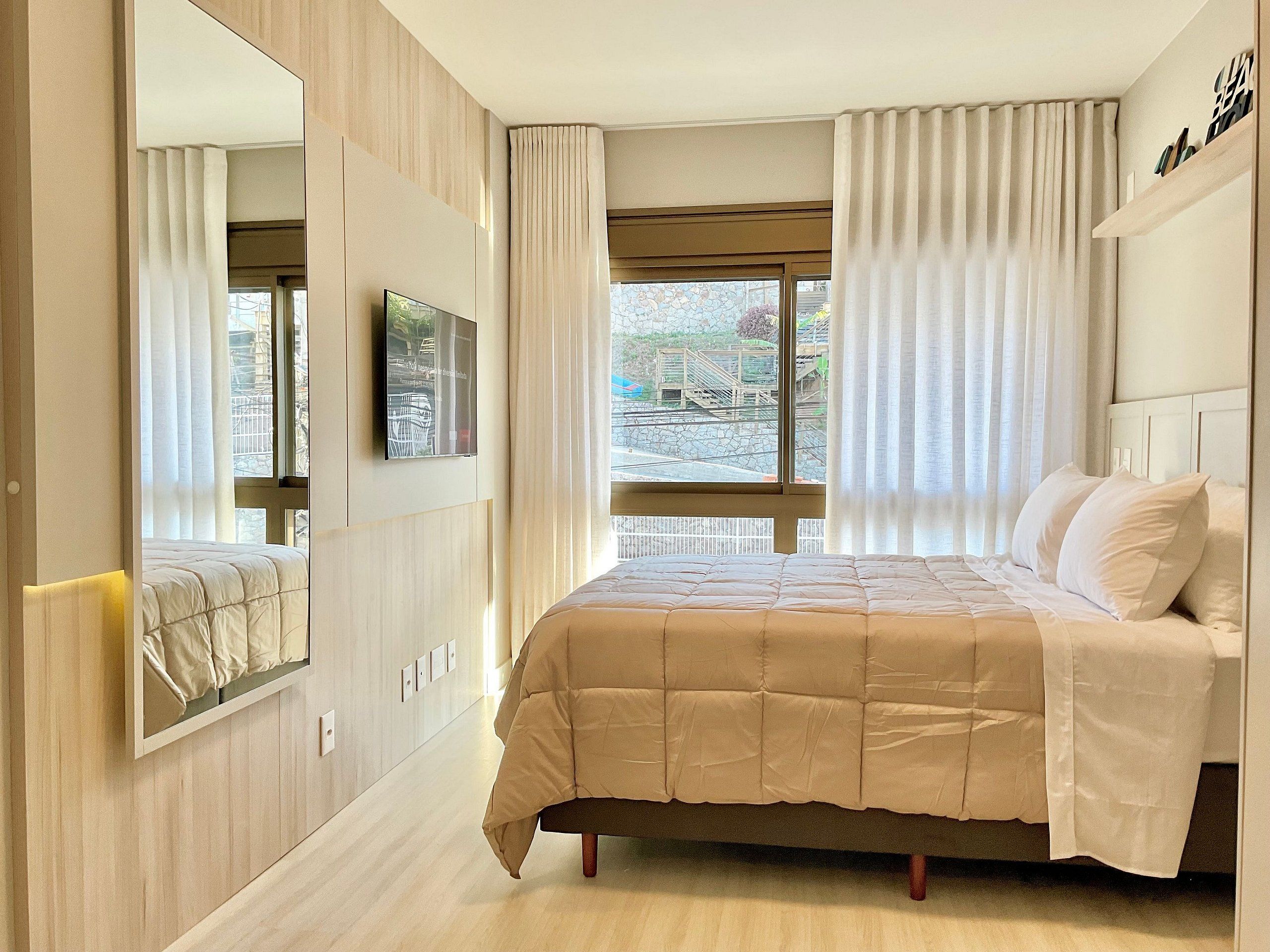 Un dormitorio con cama, televisor, ventana con cortinas y vistas al exterior.
