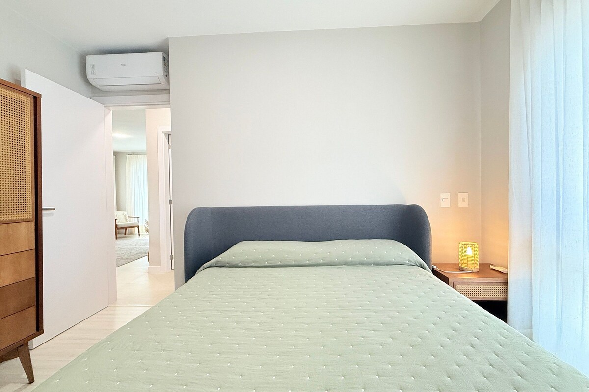 A bedroom with a bed, a wardrobe, a bedside table with a lamp, and an air conditioning unit on the wall.