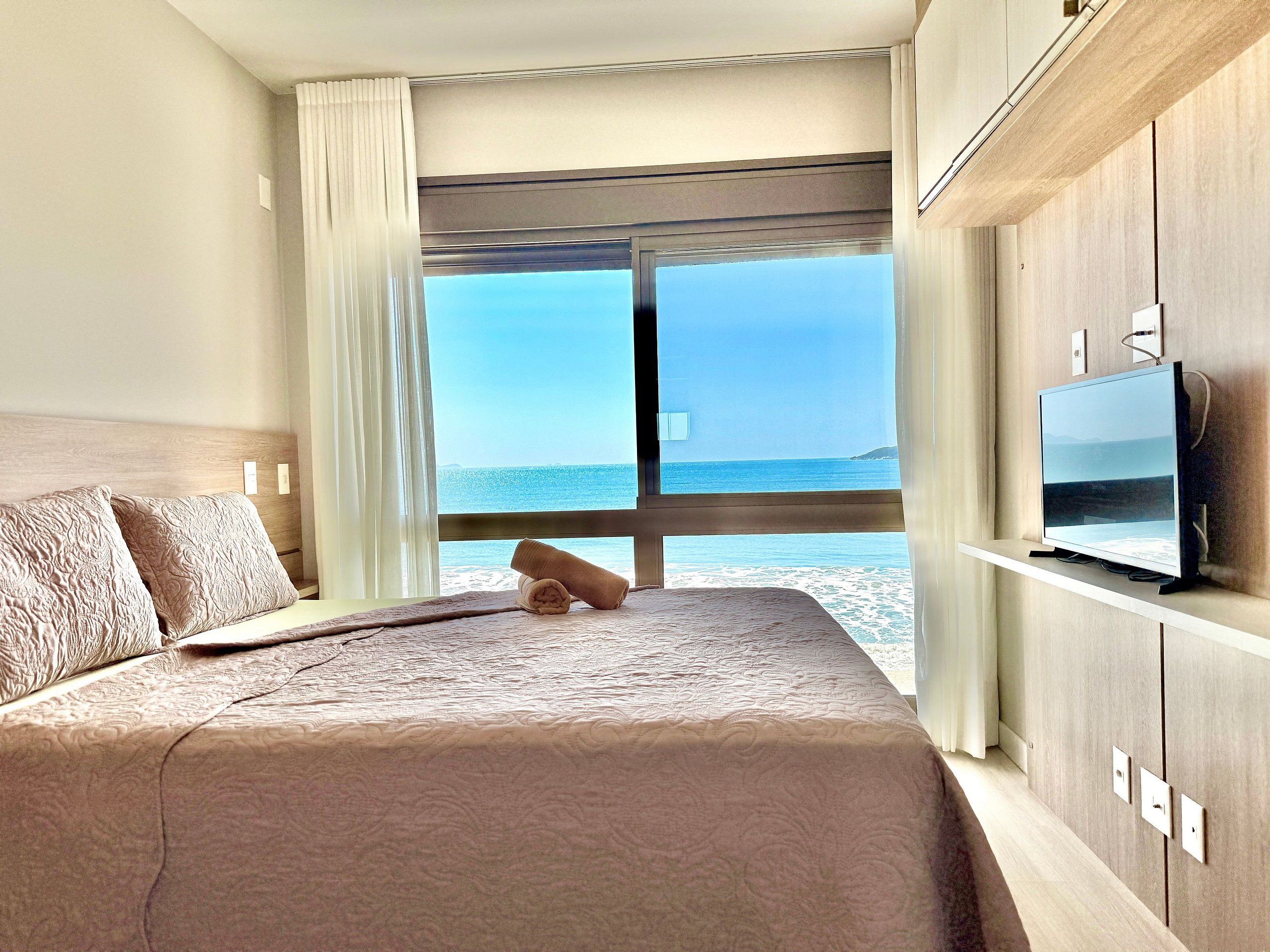 A hotel room with a bed, a TV, and a view of the sea.