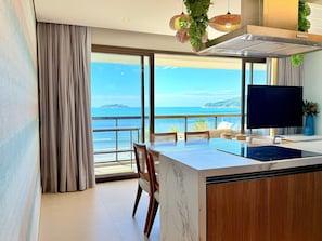 Una cocina moderna con una isla grande, un comedor con sillas, un televisor y vista al mar.