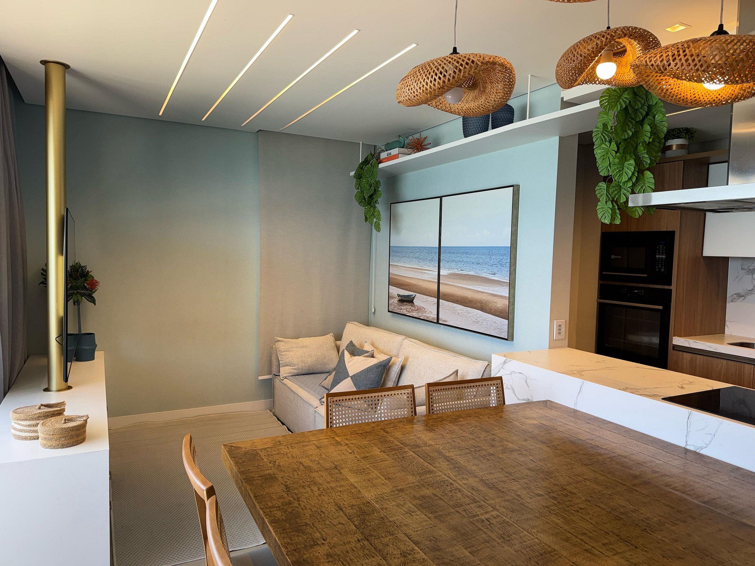 Una cocina moderna con horno integrado, un comedor con mesa y sillas de madera, y una sala de estar con sofá y un cuadro con motivos marinos.