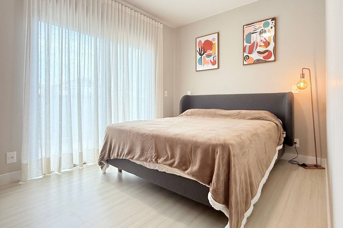 A bedroom with a bed, curtains, two wall art pieces, and a bedside lamp.