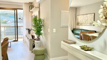 Una habitación de hotel moderna con balcón, zona de comedor y sala de estar con un espejo grande y obras de arte.