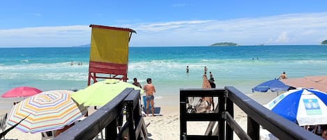 A wooden pier leading to a beach with umbrellas and a lifeguard tower.
