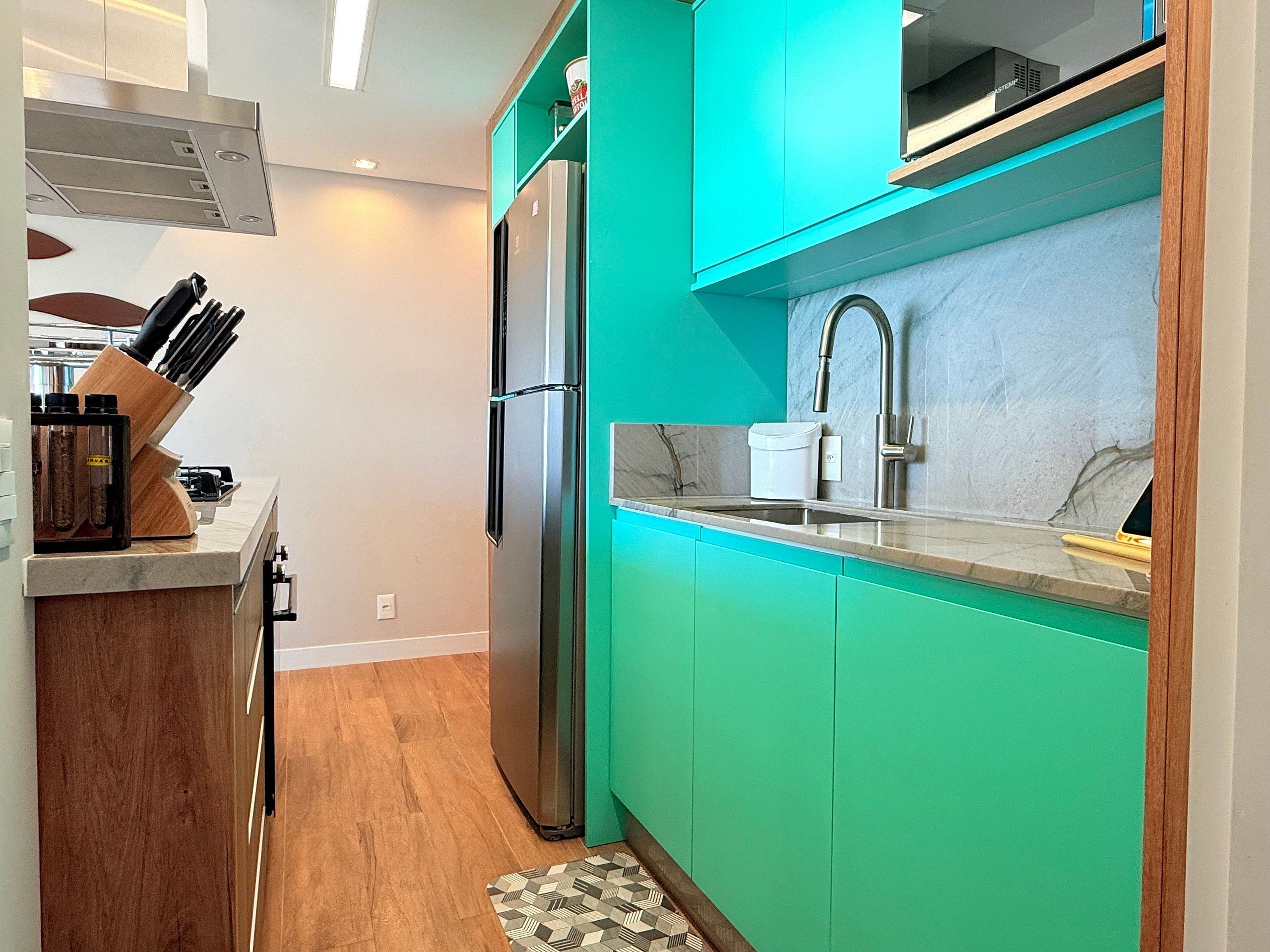 A kitchen with teal cabinets, a stainless steel refrigerator, a sink, and a patterned rug.