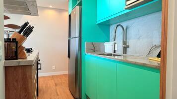 A kitchen with teal cabinets, a stainless steel refrigerator, a sink, and a patterned rug.