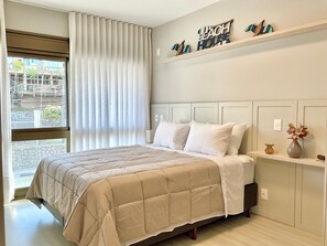 Ein Schlafzimmer mit Bett, Vorhängen am Fenster, einem Kopfteil, einem Nachttisch mit einer Vase und einer Wanddekoration.