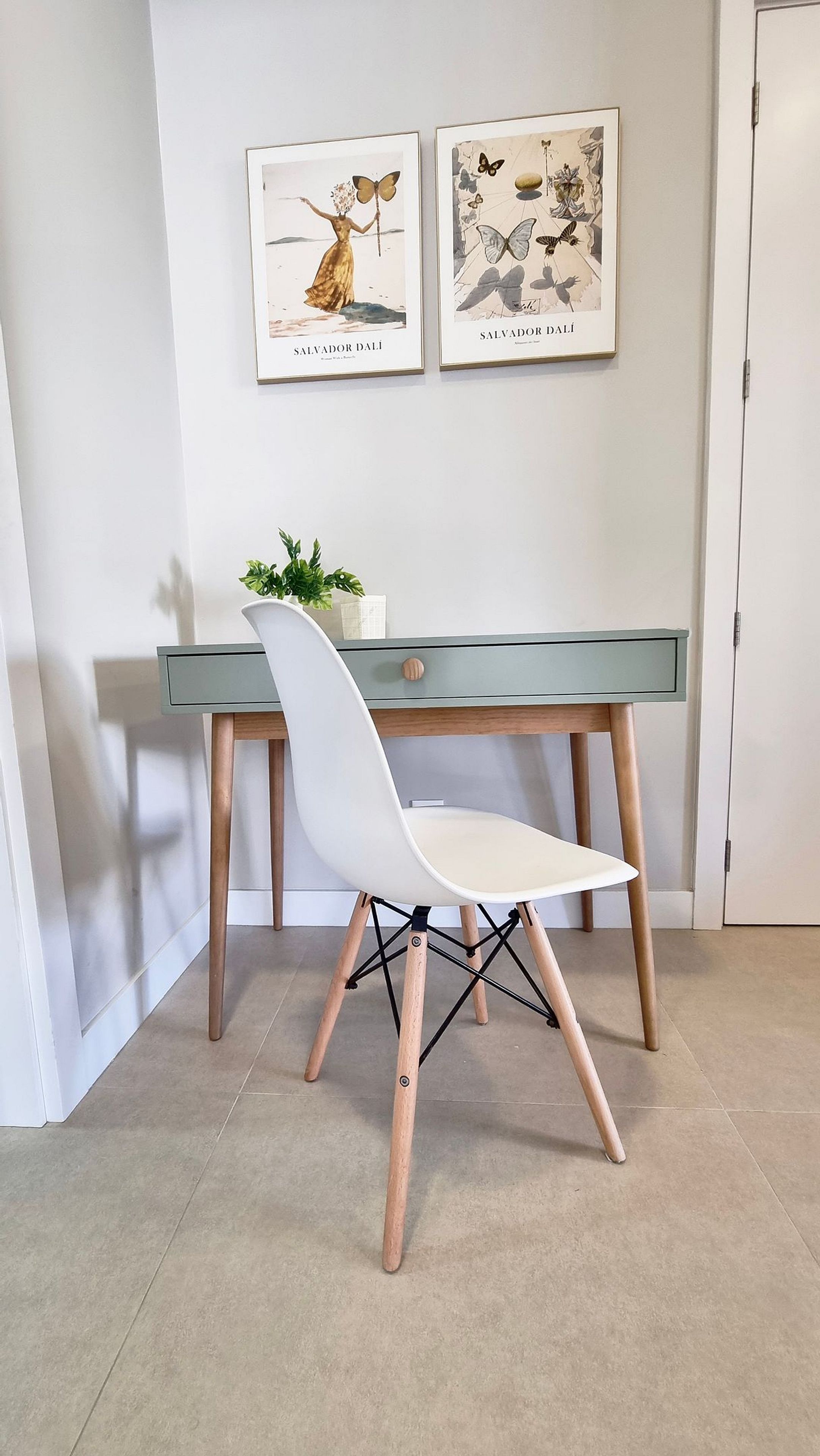 A modern room with a desk, a white chair, and two framed artworks on the wall.