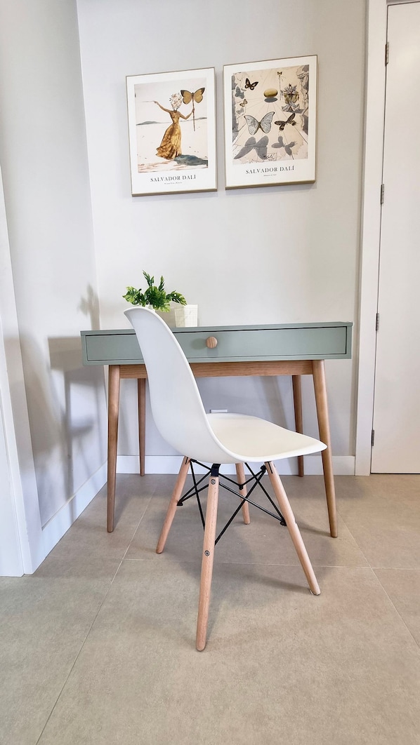 Una habitación moderna con un escritorio, una silla blanca y dos cuadros enmarcados en la pared.