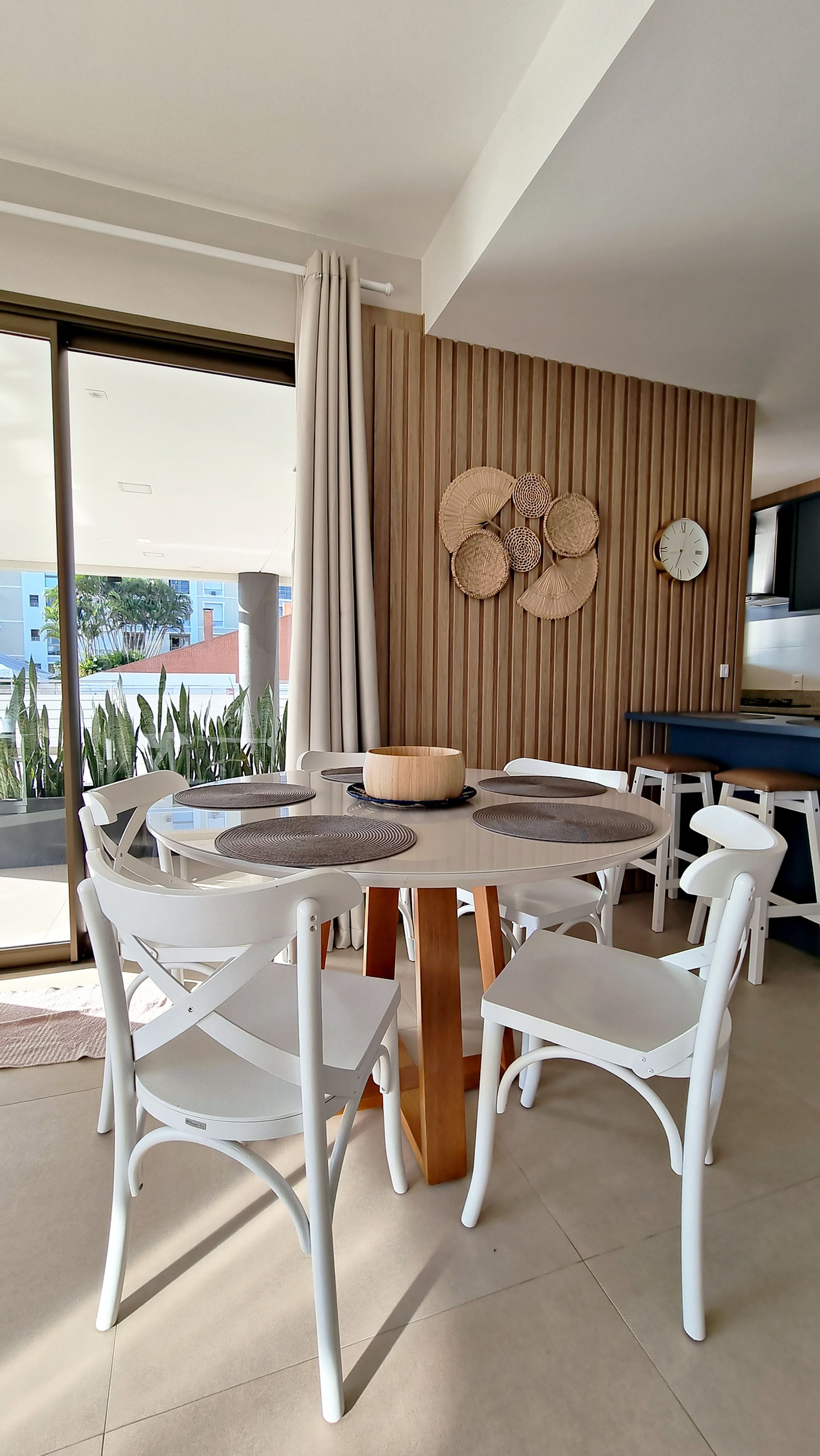 A modern dining area with a round table, white chairs, a wooden block base, and a wall-mounted clock.