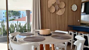 A modern dining area with a round table, white chairs, a wooden block base, and a wall-mounted clock.