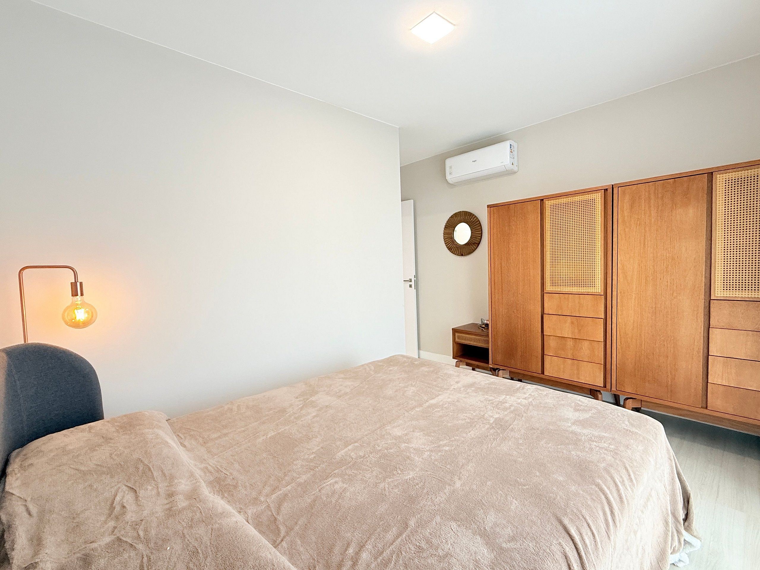 A bedroom with a bed, a wardrobe, a bedside lamp, and an air conditioning unit.