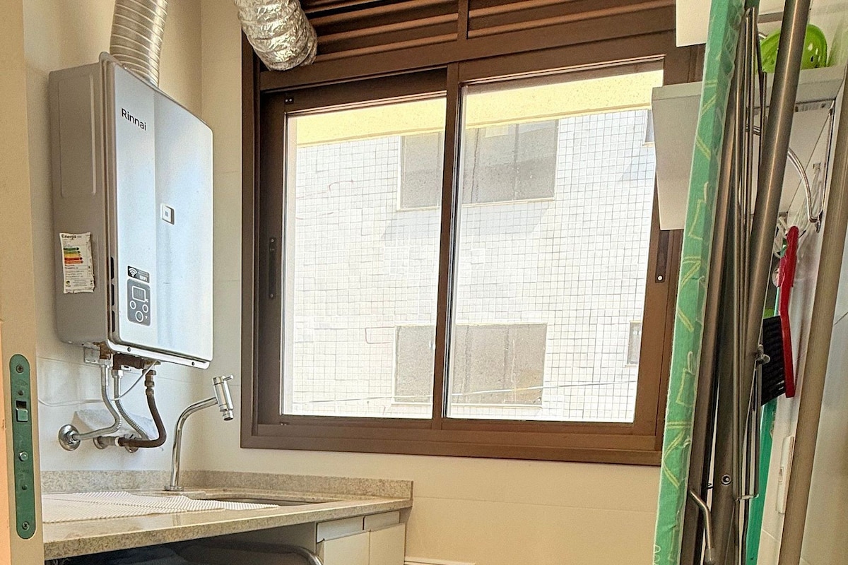 Un lavadero pequeño con lavadora, una ventana y un tendedero de metal.