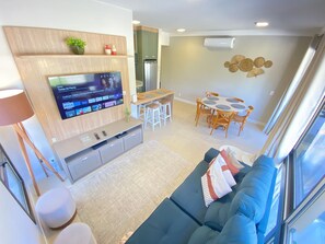 Ein modernes Wohnzimmer mit Fernseher, Sofa, Esstisch und Stühlen.