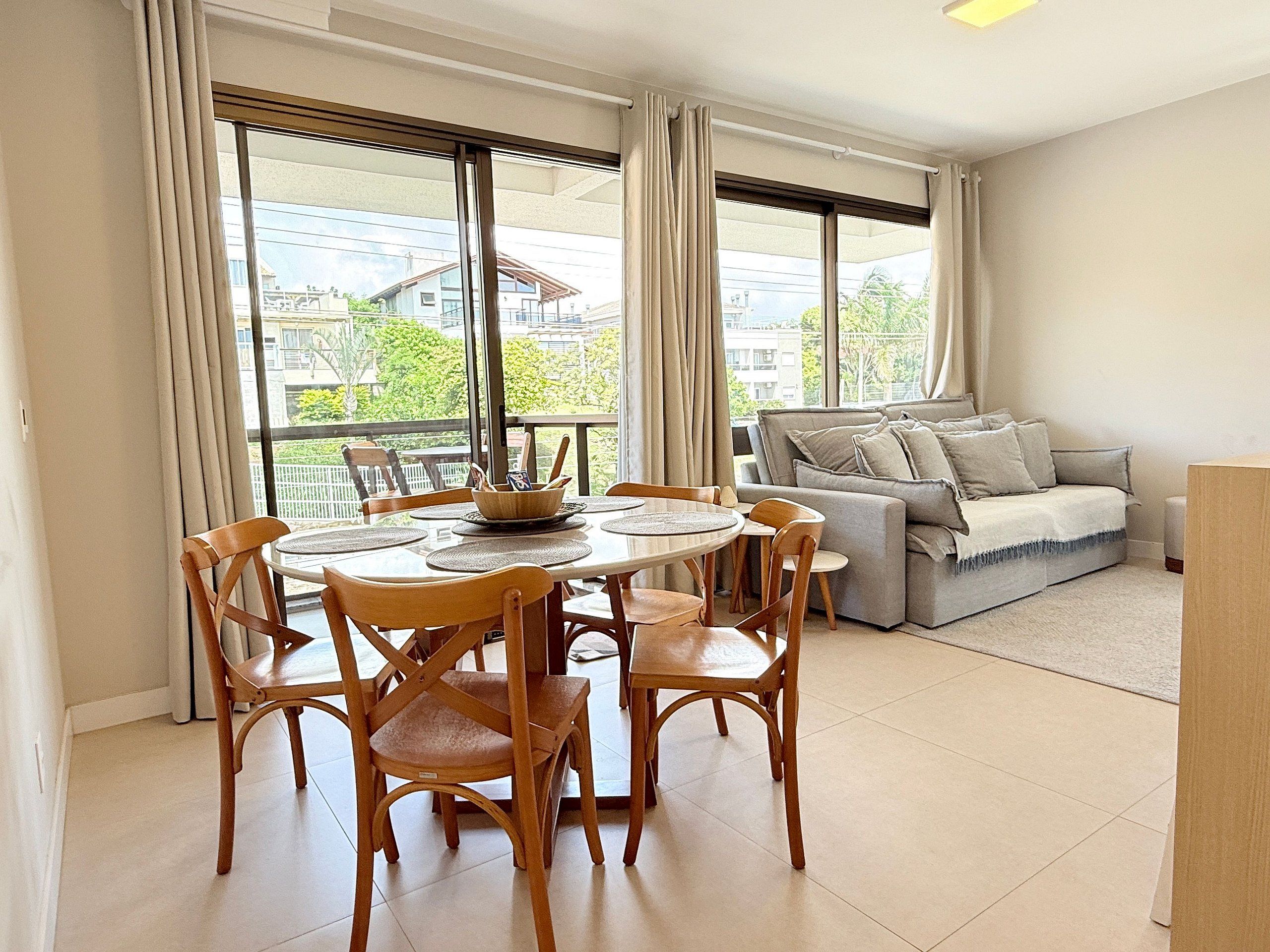A dining area with a round table and chairs, a sofa, and large windows with curtains.