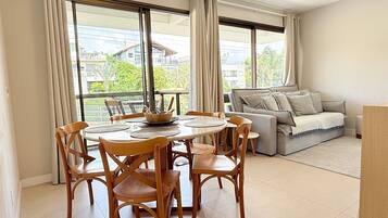 A dining area with a round table and chairs, a sofa, and large windows with curtains.