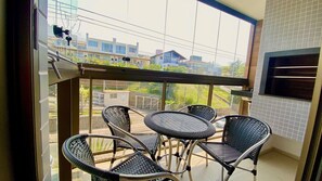 A balcony with a table and chairs, a view of buildings, and a tiled wall. - Res Belvedere Beach Garden (Florianópolis)