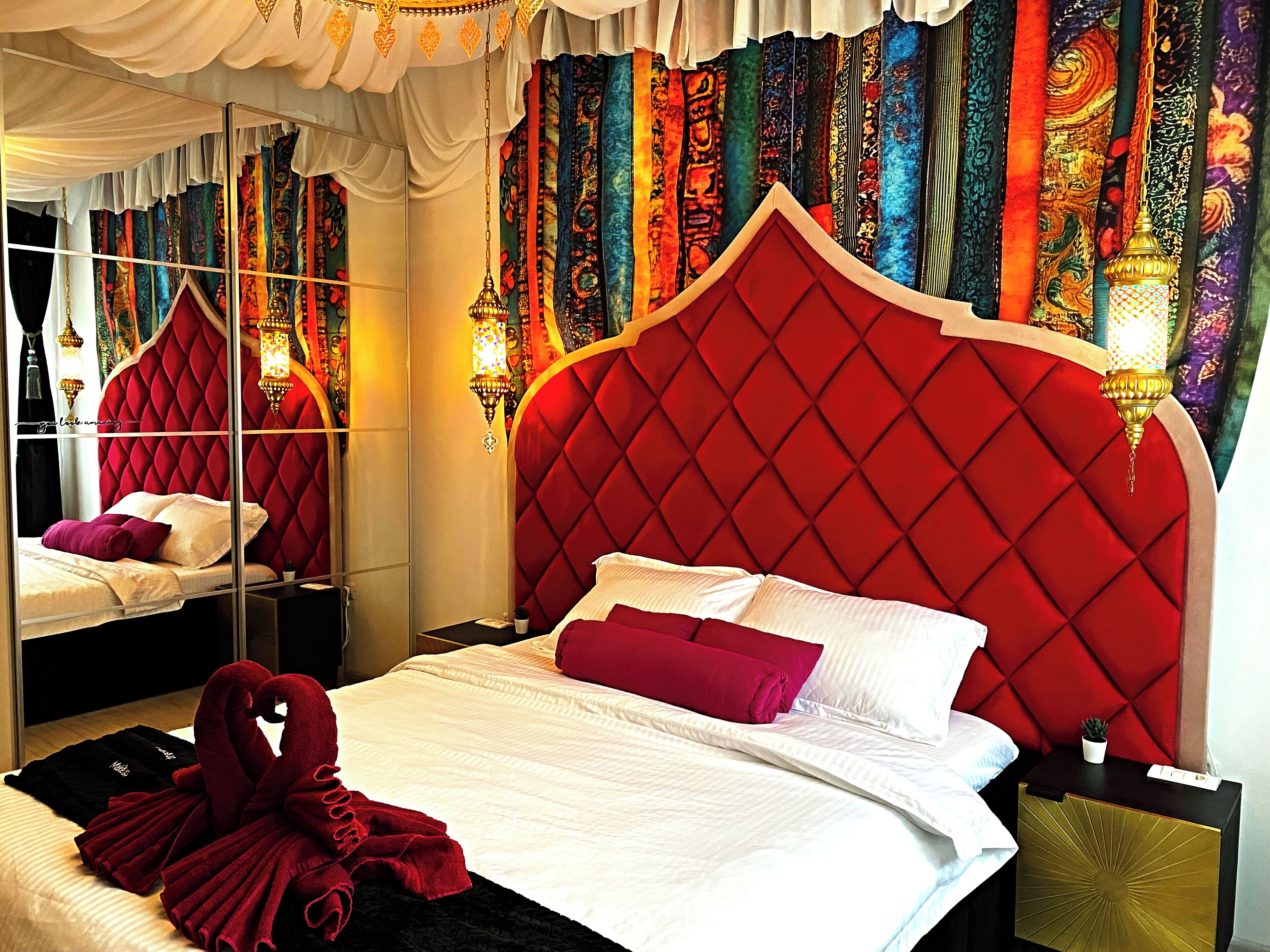 Habitación de hotel con cabecera roja, ropa de cama blanca y un espejo que refleja la habitación.