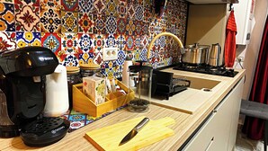 Una cucina con un vivace rivestimento in piastrelle, una macchina da caffè Bosch, un distributore di capsule Tassimo, un tagliere di legno con un coltello e un lavello.