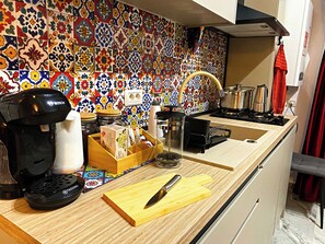 Una cocina con un salpicadero de azulejos coloridos, una cafetera, una tabla de cortar con un cuchillo y varios utensilios de cocina.