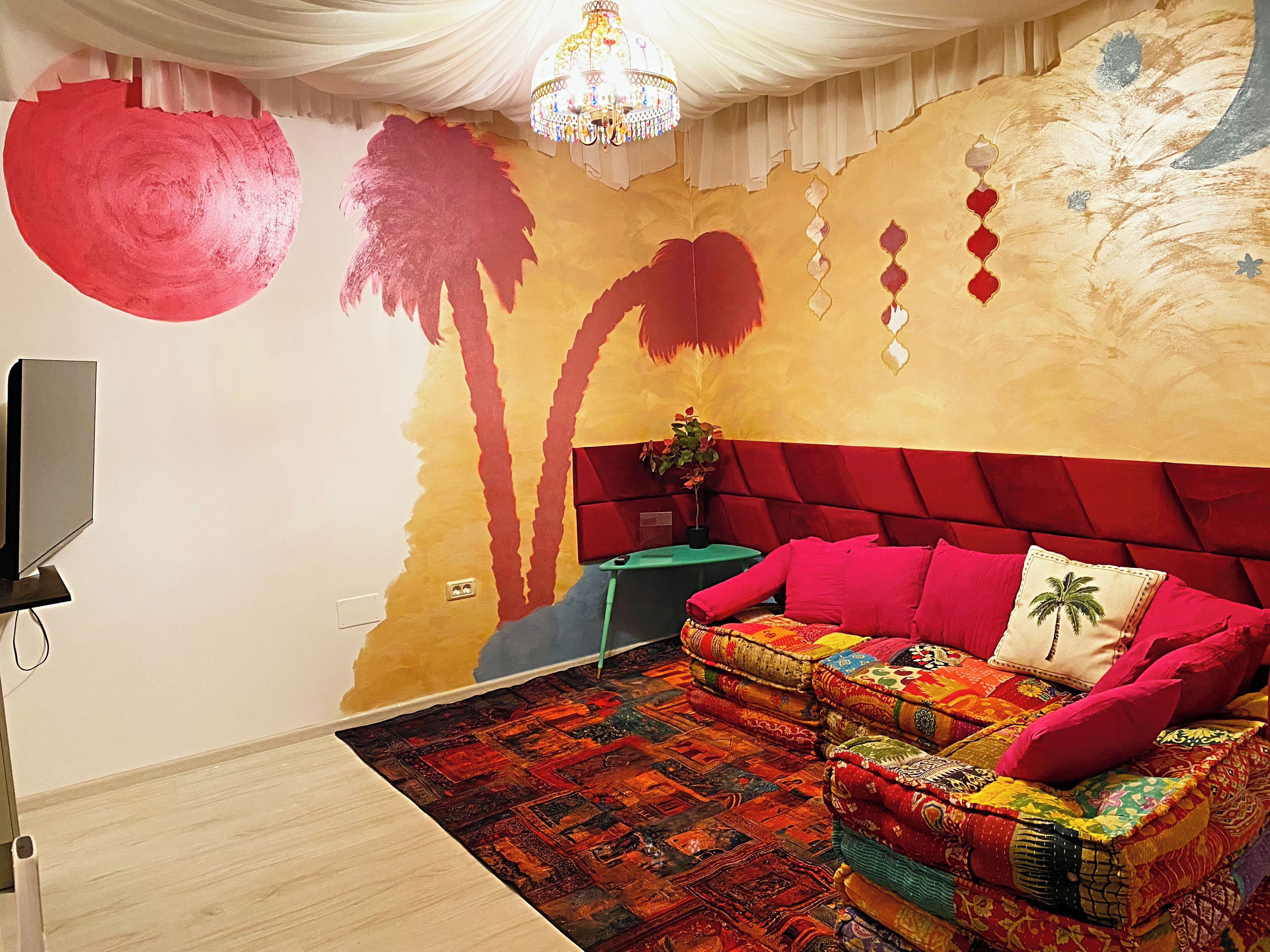 Una stanza con un divano rosso, un tappeto decorato, una televisione e un muro con un murale rosso e giallo.